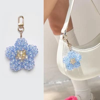 A sky blue flower of faceted glass beads with a yellow center, on a gold-tone clasp, and the same keychain on a white handbag