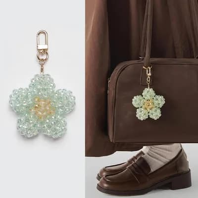 A mint flower of faceted glass beads with a yellow center, on a gold-tone clasp, and the same keychain on a brown handbag