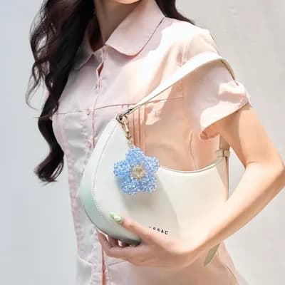 The sky blue flower keychain on the strap of a white shoulder bag