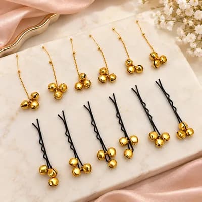 Gold chain pins and black bobby pins, each hung with a cluster of three small gold bells, on marble