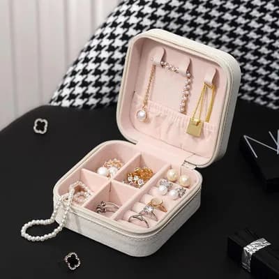 An open white mini jewelry box with necklaces on the lid hooks and earrings and rings in its compartments