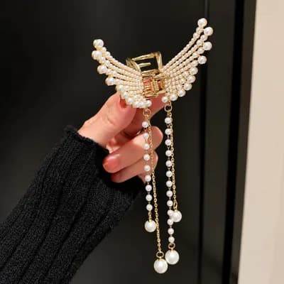 A hand holding the pearl wing claw clip, its pearl strands hanging below