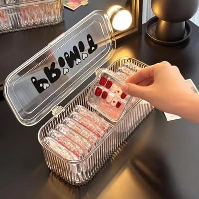 A hand lifting a small clear box of red press-on nails out of the open case