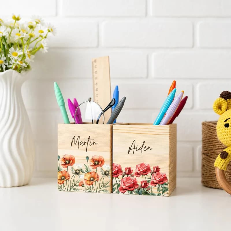 Two wooden pen holders printed with red and orange flowers and the names Martin and Aiden, holding pens and a ruler