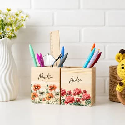 Two wooden pen holders printed with red and orange flowers and the names Martin and Aiden, holding pens and a ruler