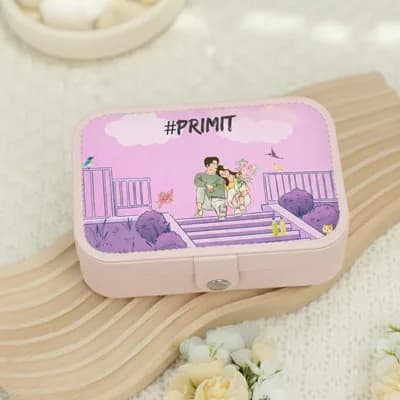 A pink jewelry box printed with a couple on a terrace among purple bushes, with “#PRIMIT” above them