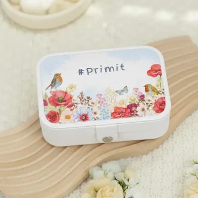 A white jewelry box printed with red poppies, blue flowers and two robins, with “#Primit” in script