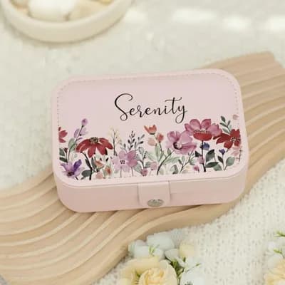 A pink jewelry box printed with “Serenity” in script above red and purple wildflowers