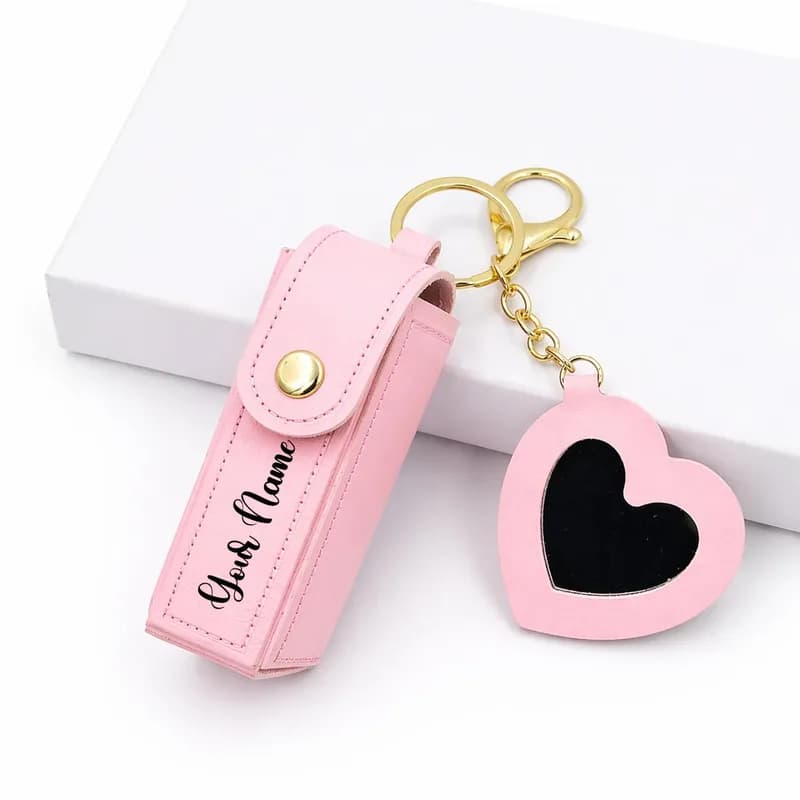A pink lipstick case printed with “Your Name”, on a gold key ring with a pink heart mirror charm