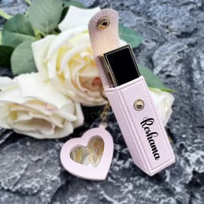 A pink case printed with the name Reshma, a lipstick inside, with its heart mirror charm, on a stone among white roses