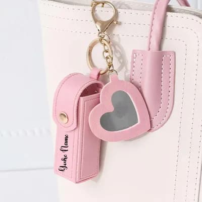 The pink keychain clipped to the handle of a cream handbag