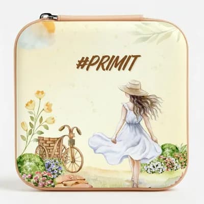 A cream mini jewelry box printed with a girl in a white dress and sun hat walking past a bicycle and flowers, with “#PRIMIT” above her
