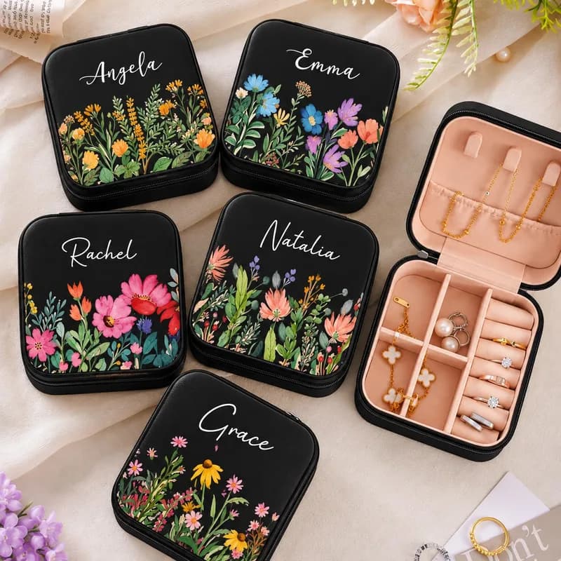 Five black mini jewelry boxes, each printed with a different flower style and a name in white script, beside an open box holding jewelry