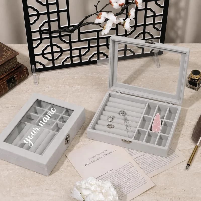 Two gray velvet jewelry boxes: one closed with “your name” in white script on the glass lid, one open with rings and a pendant