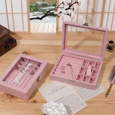 Two pink velvet jewelry boxes: one closed with “your name” in white script on the glass lid, one open with rings and a pendant