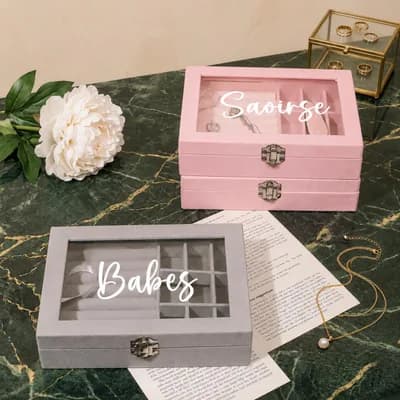 A pink box printed “Saoirse” and a gray box printed “Babes” in white script on their glass lids