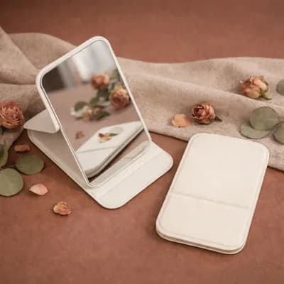 An open cream mirror on its stand beside its plain closed cover, among dried roses