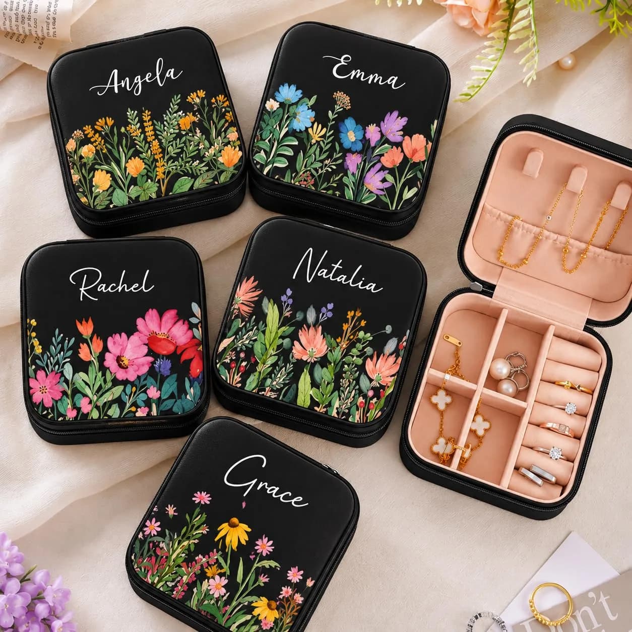 Five black mini jewelry boxes, each printed with a different flower style and a name in white script, beside an open box holding jewelry