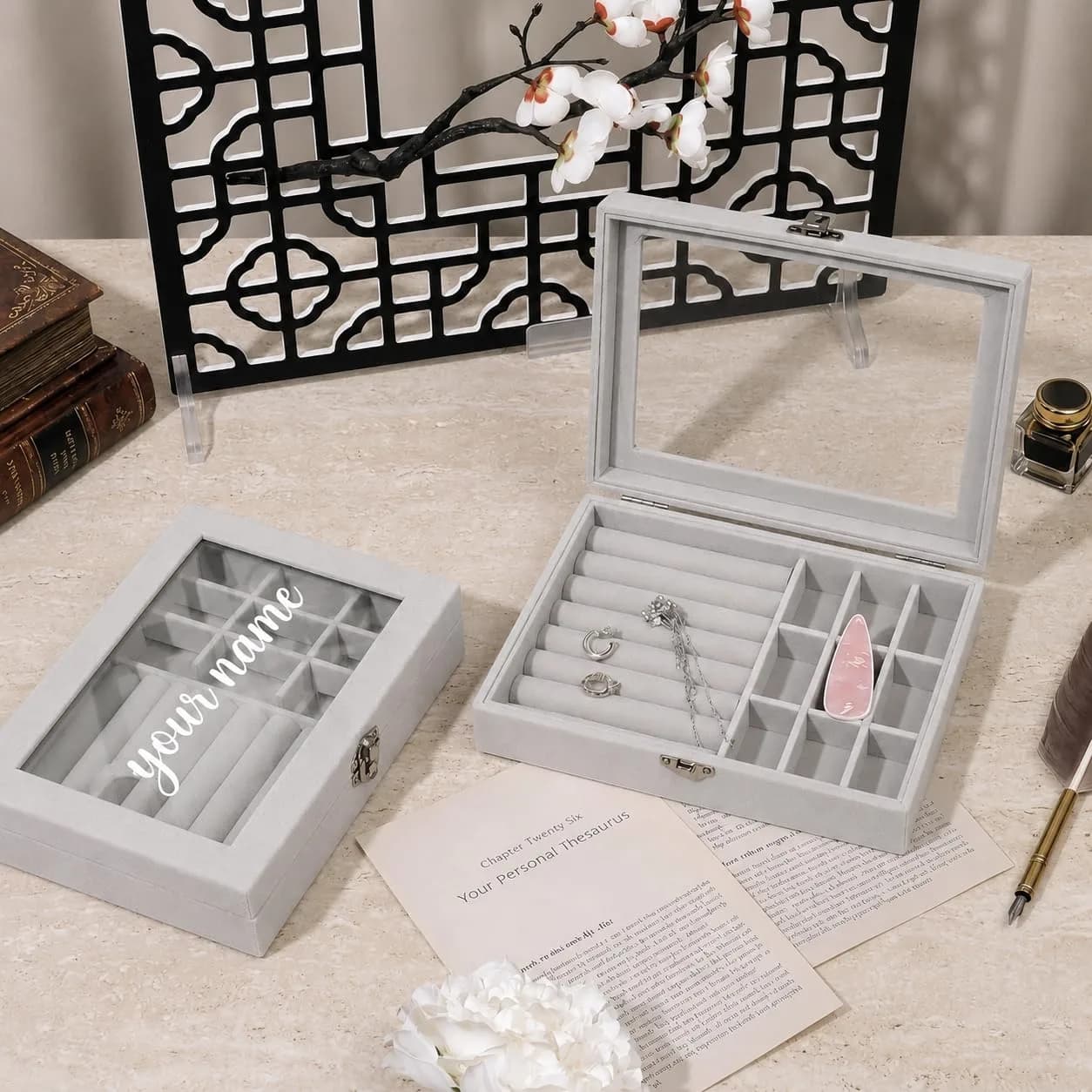 Two gray velvet jewelry boxes: one closed with “your name” in white script on the glass lid, one open with rings and a pendant